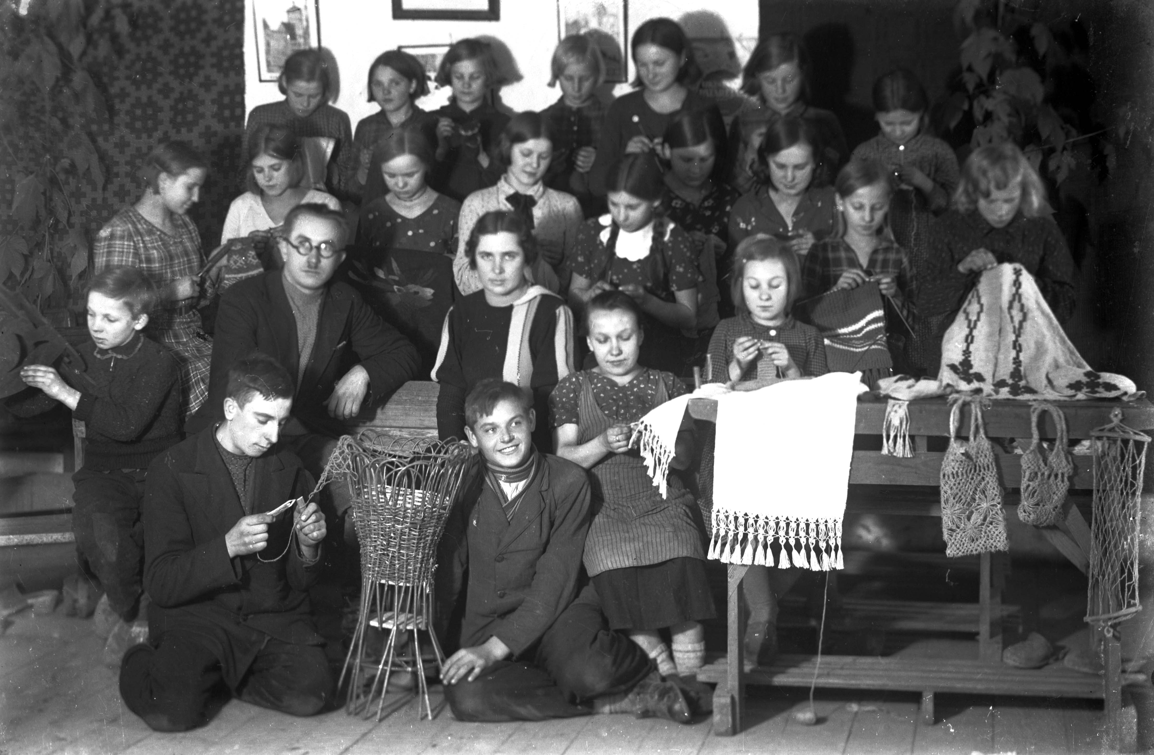 Mokytojas Kasparas Velička (su akiniais) su mokiniais, demonstruojančiais rankdarbius. Veliuona. XX a. 4 deš. Fot. A. Mickus. Veliuonos krašto istorijos muziejaus archyvo nuotr.
